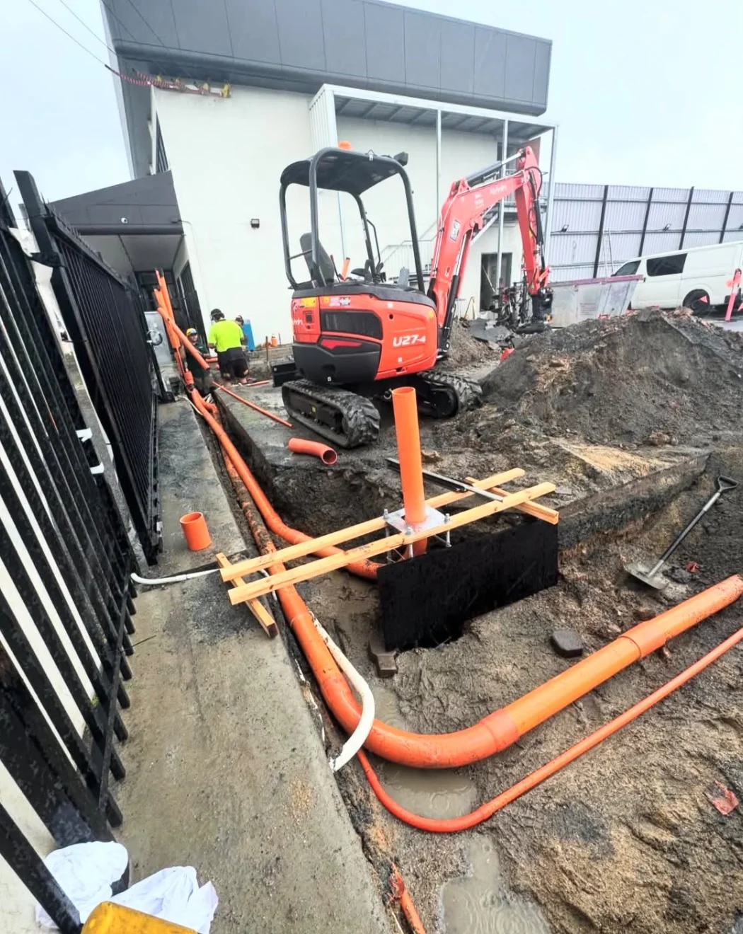 Overview of an excavator beside an open trench and orange underground conduits